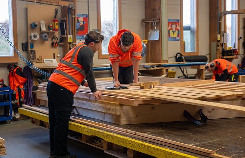 Workers in a timber workshop measuring and preparing structural beams