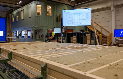 A timber floor panel on the production line, with production data displayed on a screen behind it