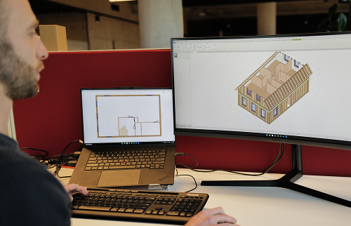 A designer reviewing a 3D timber-frame model and floor plan across two monitors